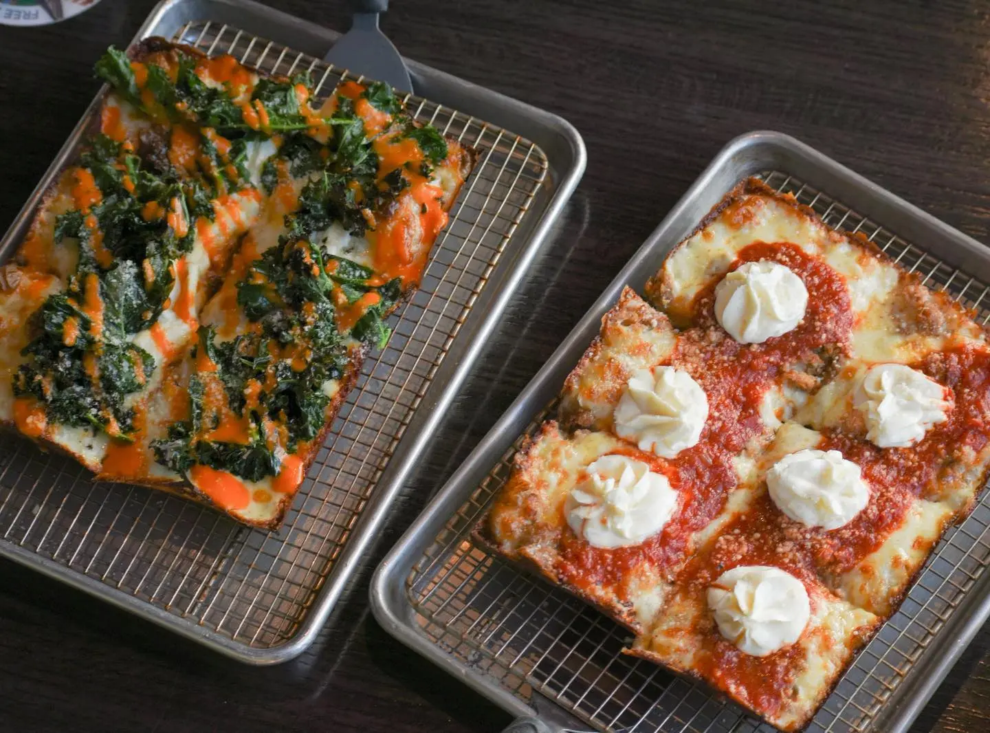 Two Detroit-style pizzas fresh from the pan: one with spinach, mushrooms and marinara, one with ricotta dollops over red sauce.